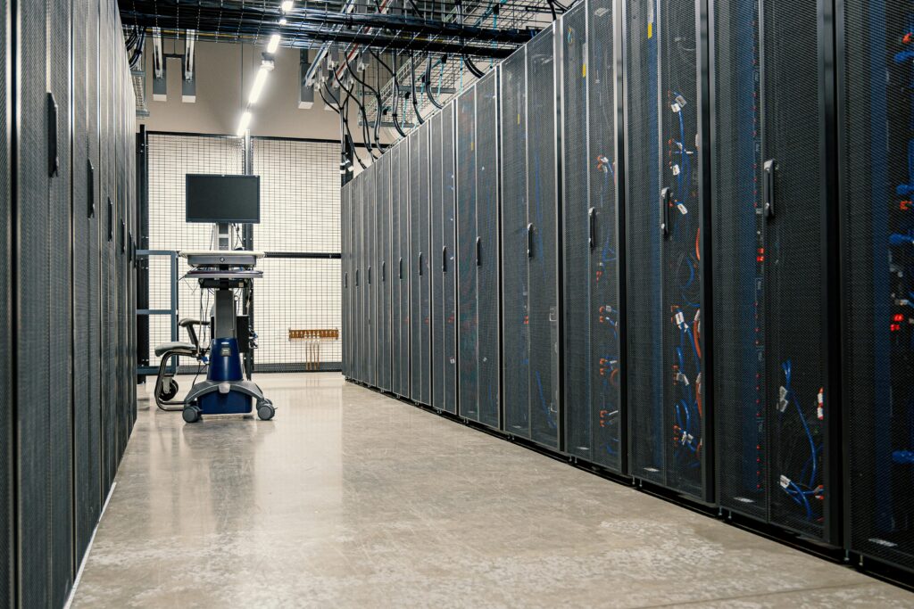 Data center aisle with rows of cooling server racks on both sides and a maintenance cart with a monitor in the middle.